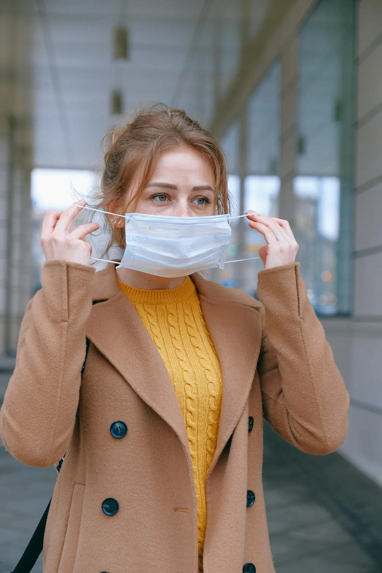 Woman adjusting her face mask on a city street, emphasizing health and protection.